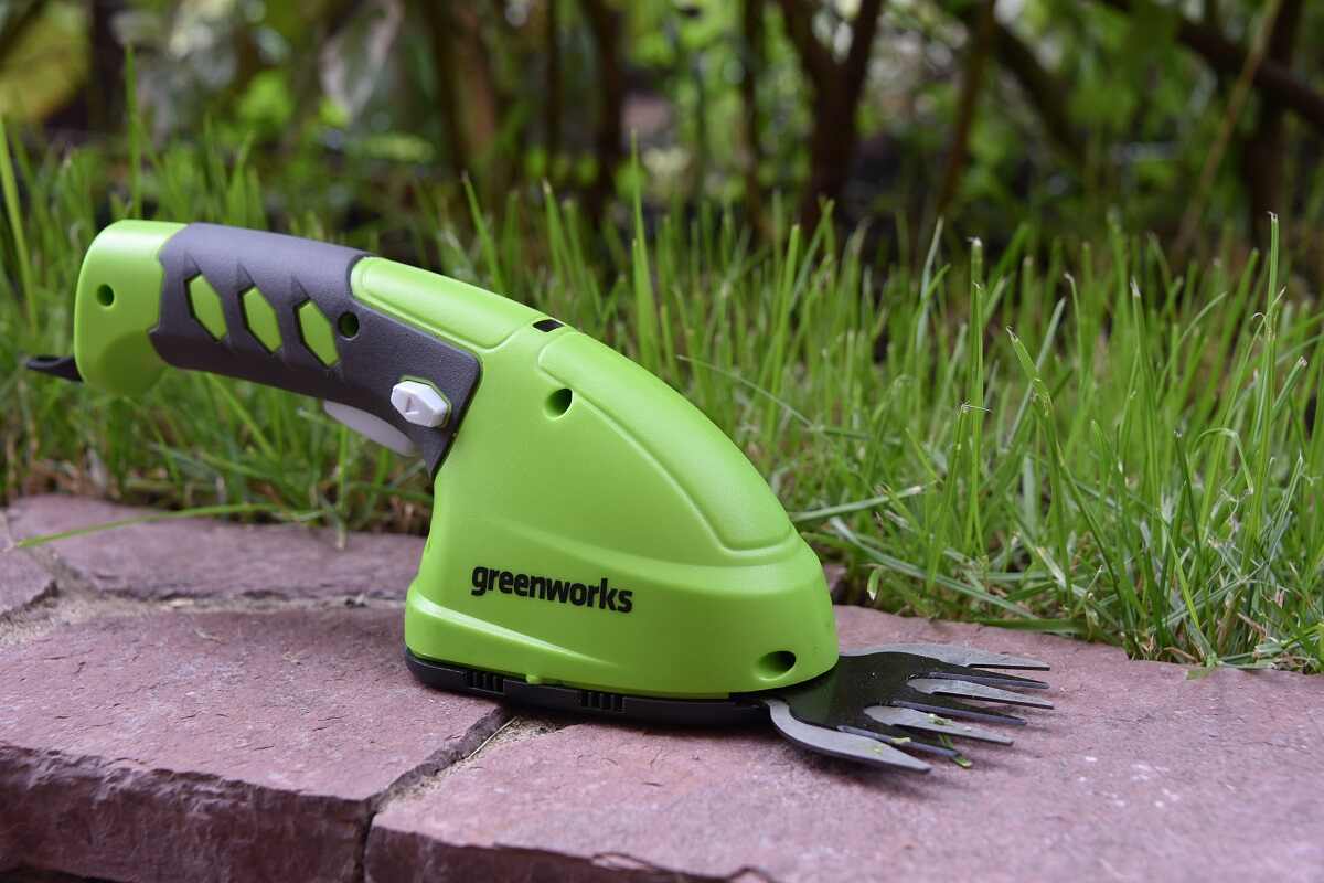 садовые ножницы-кусторез Greenworks 3,6 В на фоне травы и дерна
